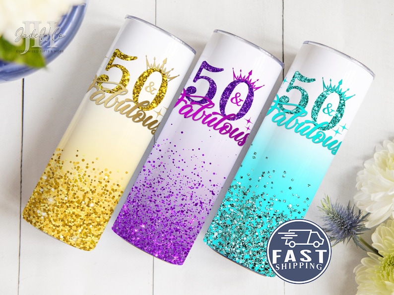 May include: Three 20 oz. stainless steel tumblers with a glitter ombre design. The tumblers are decorated with the text "50 & Fabulous" in gold, purple, and turquoise glitter.