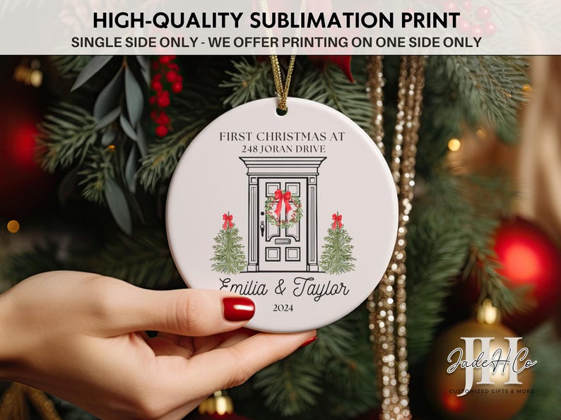May include: White ceramic Christmas ornament with a black and white illustration of a house door with a wreath and two small Christmas trees. The text "First Christmas at 248 Joran Drive" is above the door and "Emilia & Taylor 2024" is below the door.