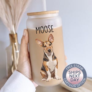 May include: A clear reusable tumbler with a brown lid and a straw. The tumbler has a cartoon image of a brown and white dog with the word "MOOSE" printed on the front.