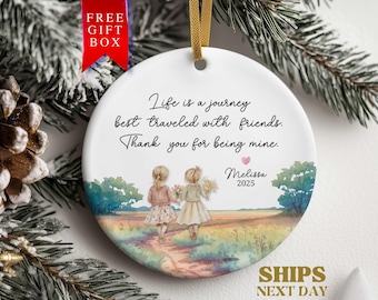 May include: White ceramic ornament with a watercolor illustration of two girls walking on a path. The ornament has the text "Life is a journey best traveled with friends. Thank you for being mine." and "Melissa 2025". A gold ribbon is attached.