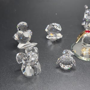 May include: A collection of clear crystal figurines, including a penguin, an angel, and a shell. The figurines are faceted, reflecting light. The penguin has small black eyes. The angel has wings and a halo. The shell is open.