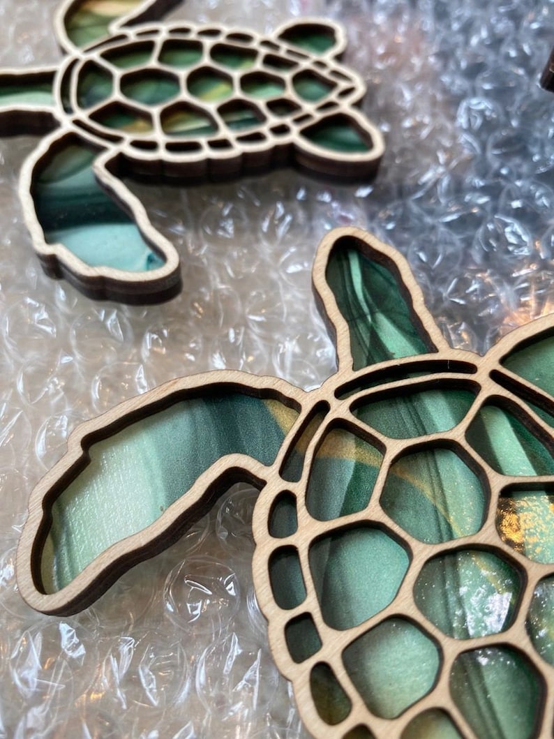 Puede incluir: Dos adornos de tortuga de madera con un dise&ntilde;o de m&aacute;rmol verde y dorado. Las tortugas est&aacute;n recortadas y tienen un patr&oacute;n de caparaz&oacute;n detallado.