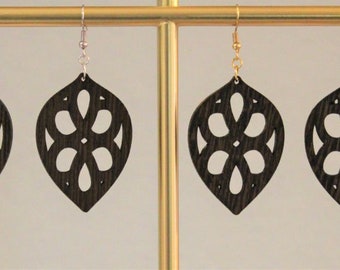 May include: Four pairs of black wooden earrings with a delicate floral design. The earrings are hanging from a gold stand.
