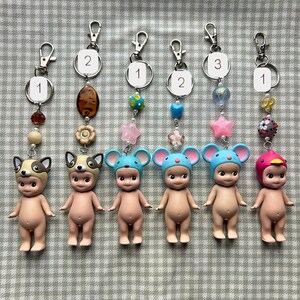 May include: Six keychains with small, nude figurines wearing animal hats. Each keychain has a silver clasp and decorative beads. The hats are designed as a dog, mouse, and bird.