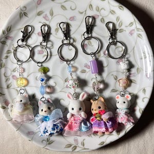 May include: Six adorable animal keychains with beaded chains and silver key rings. The animals are dressed in colorful dresses and include a rabbit, a cat, a mouse, and three other animals.