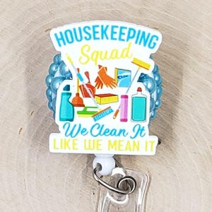 May include: A Housekeeping Squad badge reel with the text "Housekeeping Squad We Clean It Like We Mean It." The badge reel features cleaning supplies and blue accents. The reel is attached to a clear plastic holder.