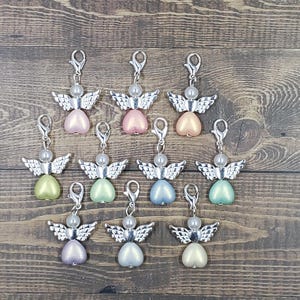 Peut inclure: Une collection de breloques en forme d'ange avec des ailes et des fermoirs argent&eacute;s. Chaque breloque pr&eacute;sente un corps en forme de c&oelig;ur de diff&eacute;rentes couleurs pastel, dont le rose, le vert et le bleu, surmont&eacute; d'une perle.