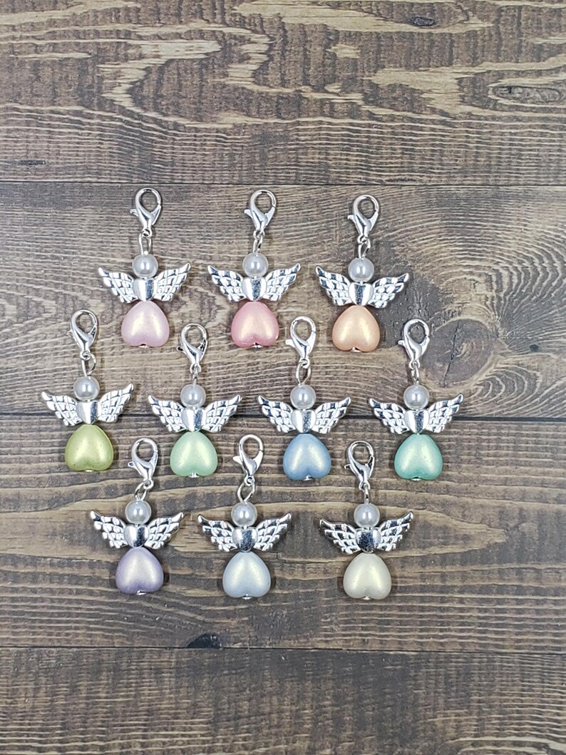 Peut inclure: Une collection de breloques en forme d'ange avec des ailes et des fermoirs argent&eacute;s. Chaque breloque pr&eacute;sente un corps en forme de c&oelig;ur de diff&eacute;rentes couleurs pastel, dont le rose, le vert et le bleu, surmont&eacute; d'une perle.