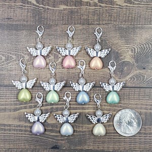 Peut inclure: Collection de breloques en forme d'ange avec des ailes et des fermoirs argent&eacute;s. Chaque breloque pr&eacute;sente un corps en forme de c&oelig;ur nacr&eacute; de diff&eacute;rentes couleurs pastel, surmont&eacute; d'une perle. Une pi&egrave;ce de monnaie est incluse pour la r&eacute;f&eacute;rence de taille.