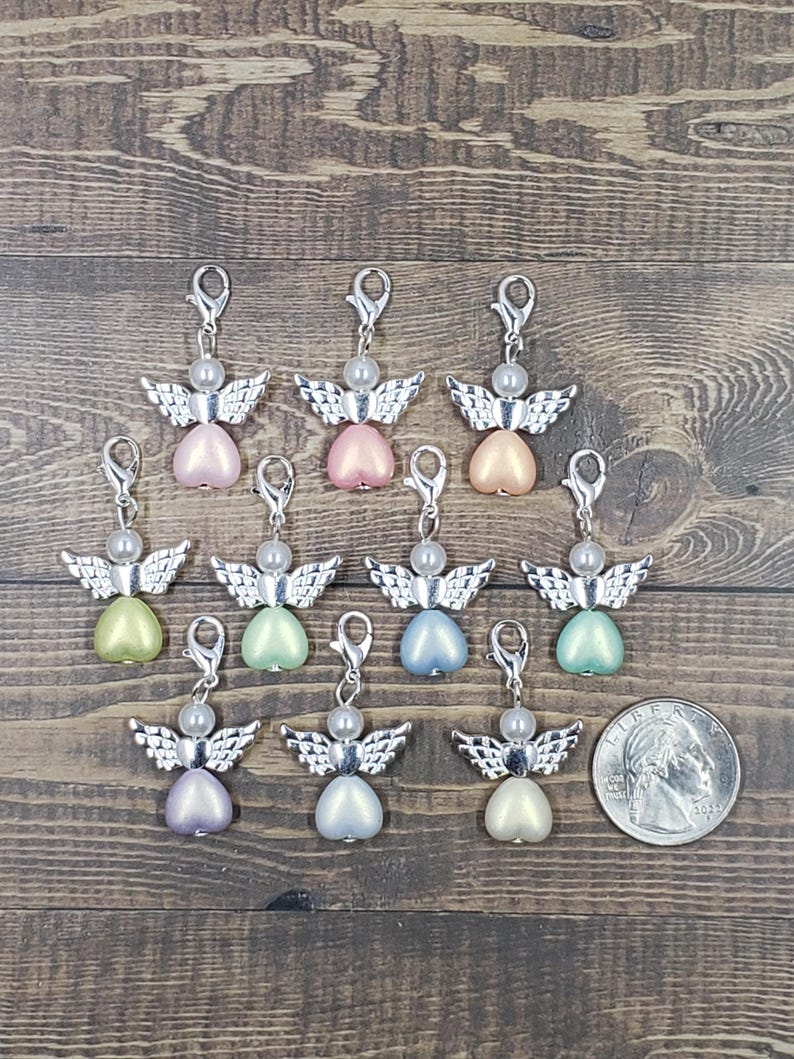 Peut inclure: Collection de breloques en forme d'ange avec des ailes et des fermoirs argent&eacute;s. Chaque breloque pr&eacute;sente un corps en forme de c&oelig;ur nacr&eacute; de diff&eacute;rentes couleurs pastel, surmont&eacute; d'une perle. Une pi&egrave;ce de monnaie est incluse pour la r&eacute;f&eacute;rence de taille.