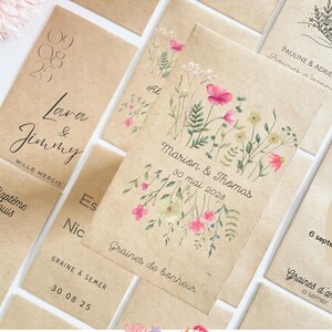 Könnte beinhalten: Eine Sammlung von Samenpäckchen aus Kraftpapier mit floralen Aquarelldesigns und handgeschriebenem Text. Die Päckchen tragen Namen, Daten und Sätze wie "Graines de bonheur" und "Graines d'amour".