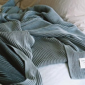以下が含まれることがあります： 青と白のストライプのニットの毛布で、タグには「Lumi Living」と書いてあります。