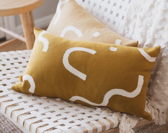 May include: Two throw pillows with abstract patterns. The bottom pillow is mustard yellow with white abstract shapes. The top pillow is a light beige with white abstract shapes.