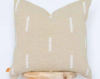 May include: A square decorative pillow with a beige and white striped pattern. The pillow has vertical white rectangular accents and is placed on a wooden stool. The pillow is a neutral color and would complement any home decor.