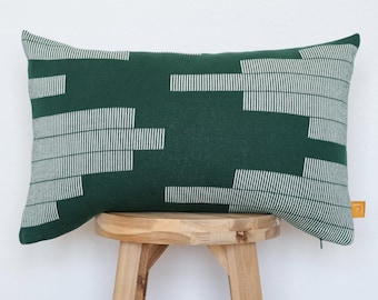 May include: A rectangular throw pillow in a deep forest green color featuring a white geometric pattern of horizontal lines of varying lengths. The pillow has a small orange fabric tag on the right side and a visible zipper along the bottom edge.