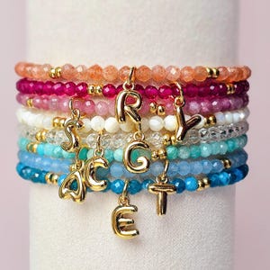 以下が含まれることがあります： ゴールドの文字チャームが付いた、マルチカラーのビーズブレスレット。ブレスレットには、ピンク、レッド、ホワイト、ブルー、グリーンなど、さまざまなビーズが使用されています。ゴールドの文字チャームは、「GRACEY」という単語を綴っています。