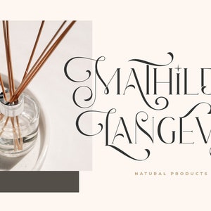 K&ouml;nnte beinhalten: Eine klare Glasflasche mit einem silbernen Deckel und braunen St&auml;bchen im Inneren. Die Flasche steht auf einer wei&szlig;en Oberfl&auml;che. Der Text "Mahilde & Langevin" ist in einer dekorativen Schriftart mit einem goldenen Blattdesign geschrieben. Der Text "Naturprodukte" steht unter dem Namen.