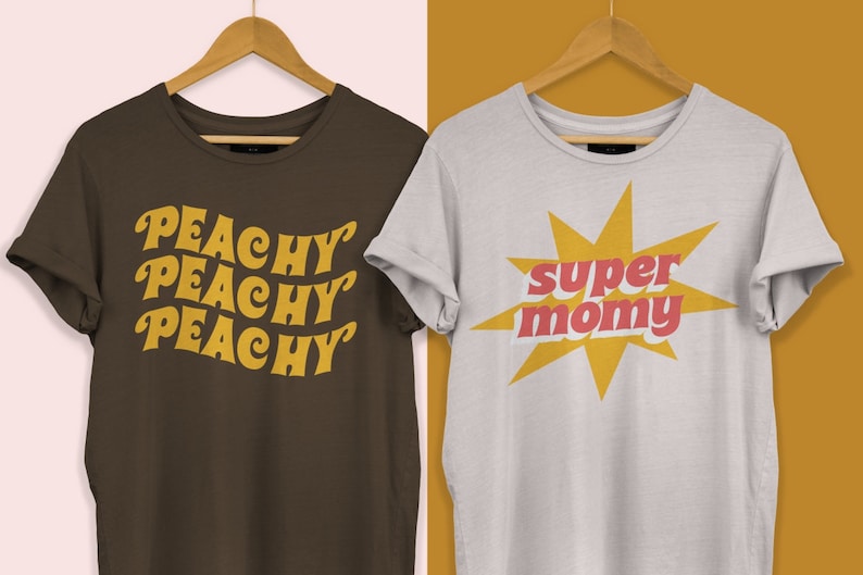以下が含まれることがあります： レトロなグラフィックがプリントされたTシャツ2枚。1枚は茶色のTシャツで、黄色で「Peachy Peachy Peachy」と書いてある。もう1枚は白いTシャツで、黄色の星形の中に赤と黄色の「super mommy」と書いてある。