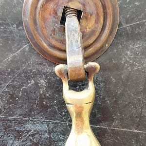 以下が含まれることがあります： 丸い土台と涙滴型のプルを持つ真鍮製のドアハンドル。ハンドルは伝統的なスタイルで、使い古したようなアンティークな仕上げになっています。