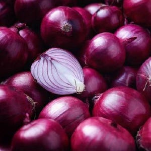 May include: A collection of whole red onions with deep purple skins, featuring one onion sliced in half to reveal its layered, translucent white and light purple interior flesh. The onions are tightly packed together, showing their round shapes.