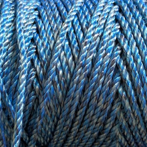 May include: A spool of twisted rope featuring a vibrant blend of bright blue and metallic silver fibers. The rope is tightly coiled, showcasing a repeating diagonal pattern created by the intertwining strands of blue and silver synthetic material.