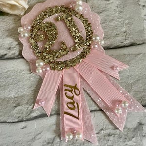 May include: Pink and gold glitter 21st birthday rosette with a pink ribbon and the name Lacy written on it.