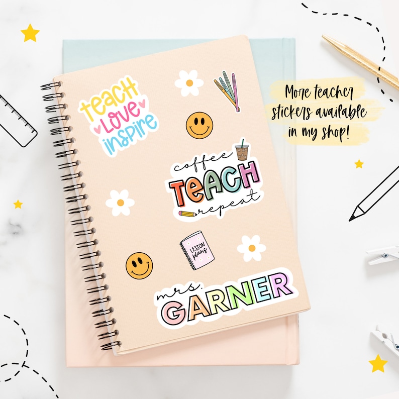 May include: A pink and peach spiral bound notebook with colorful stickers on the cover. The stickers include a coffee cup with the text "coffee teach repeat", a smiley face, a flower, a pencil, and a book with the text "lesson plans". The notebook also has a sticker with the text "teach love inspire" and a sticker with the text "mrs. GARNER".
