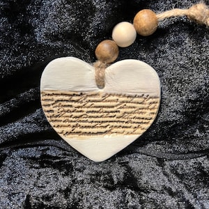 May include: White ceramic heart ornament with a brown and white striped design and a brown wood bead garland. The heart has a handwritten script pattern.