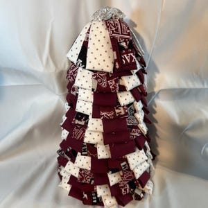Puede incluir: Un árbol de Navidad de tela hecho a mano con un diseño en capas. El árbol está hecho de cuadrados alternos de tela burdeos y blanca con lunares. La parte superior está adornada con una pieza decorativa plateada.