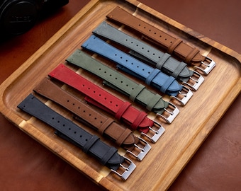 May include: Seven different coloured leather watch straps on a wooden tray. The straps are in shades of brown, grey, blue, green, and red.