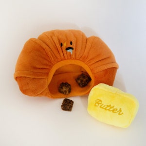May include: Orange plush toy shaped like a loaf of bread with a smiling face and the word "Butter" embroidered on a yellow plush toy.