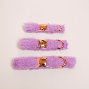 May include: Three purple faux fur dog collars with rose gold hardware and a D-ring. The collars are arranged vertically, with the smallest at the top and the largest at the bottom.