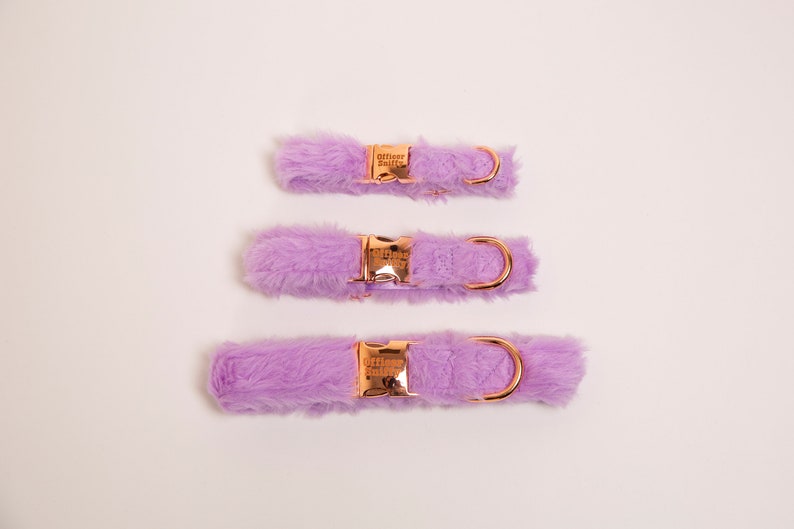May include: Three purple faux fur dog collars with rose gold hardware and a D-ring. The collars are arranged vertically, with the smallest at the top and the largest at the bottom.