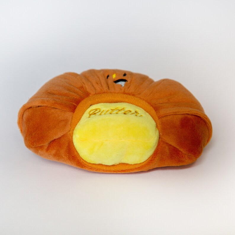 May include: A plush orange and yellow butter-shaped toy with a smiling face and the word "Butter" embroidered on the front.