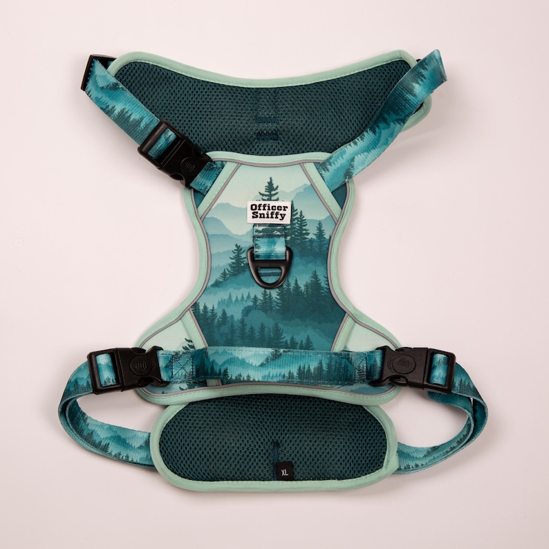 Op de afbeelding: Een teal en groene hondentuig met een bosontwerp. De tuig heeft verstelbare bandjes, zwarte gespen en de tekst "Officer Sniffy". De tuig is gemarkeerd met XL.