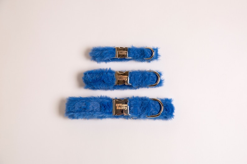 May include: Three blue faux fur dog collars with silver buckles. The buckles have the text "Officer Sniffy" engraved on them.