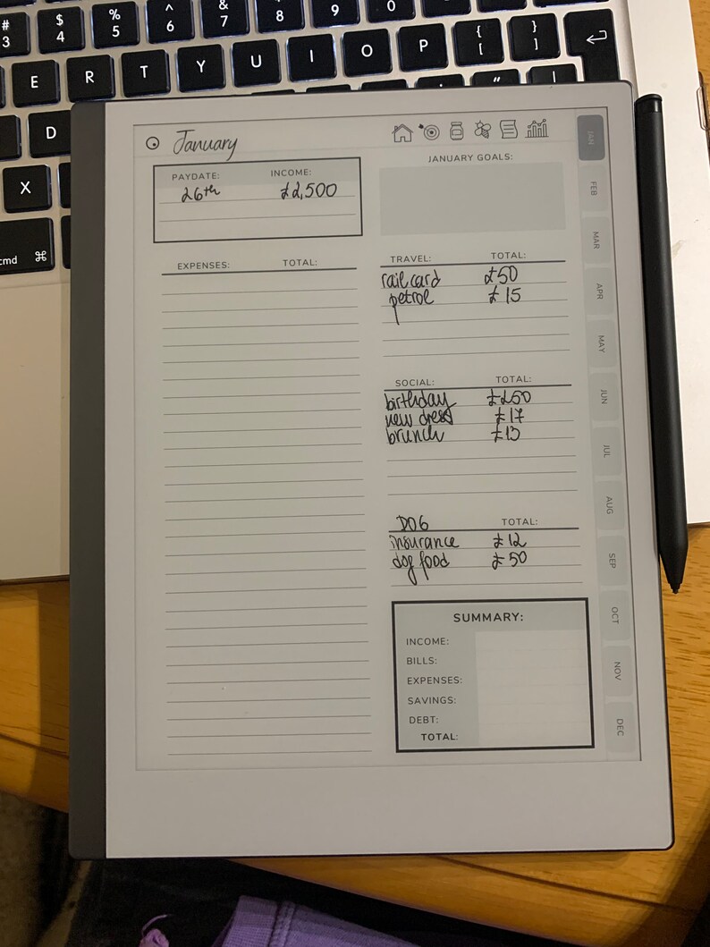 Puede incluir: Un planificador digital que muestra un presupuesto de enero con entradas manuscritas. El planificador muestra ingresos, gastos y objetivos, con un l&aacute;piz &oacute;ptico negro apoyado en el lateral. El planificador est&aacute; sobre una superficie de madera junto a un teclado de port&aacute;til.