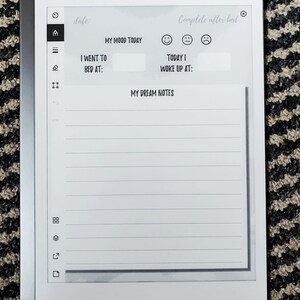 K&ouml;nnte beinhalten: Ein wei&szlig;er digitaler Notizblock mit schwarzem Rand und grauem Hintergrund. Der Notizblock hat ein Datumsfeld, einen Stimmungs-Tracker, einen Abschnitt zum Aufzeichnen der Uhrzeit, zu der Sie ins Bett gegangen sind und aufgewacht sind, und einen Abschnitt f&uuml;r Traumnotizen. Der Text auf dem Notizblock lautet "Datum:", "Nach dem Schlaf ausf&uuml;llen", "Meine Stimmung heute", "Ich bin ins Bett gegangen um:", "Heute bin ich aufgewacht um:" und "Meine Traumnotizen".