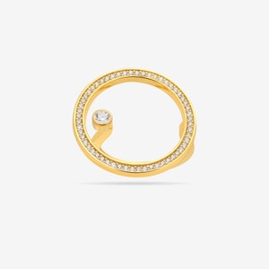 Puede incluir: Un anillo de oro con un círculo de piedras transparentes y una sola piedra transparente en un tallo curvo.