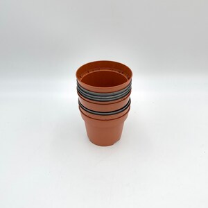 May include: A stack of four terracotta plant pots, each with a dark grey rim. The pots are stacked on a white surface.