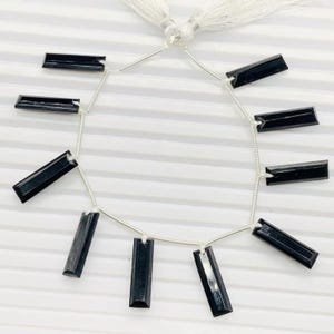 Pu&ograve; includere: Una collana di perle di pietre preziose nere, ogni perla &egrave; un prisma rettangolare con una finitura sfaccettata. Le perle sono infilate su un filo d'argento con un fiocco all'estremit&agrave;.