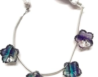 May include: A strand of iridescent purple, blue, and green fluorite flower beads on a silver chain with white tassels at each end.