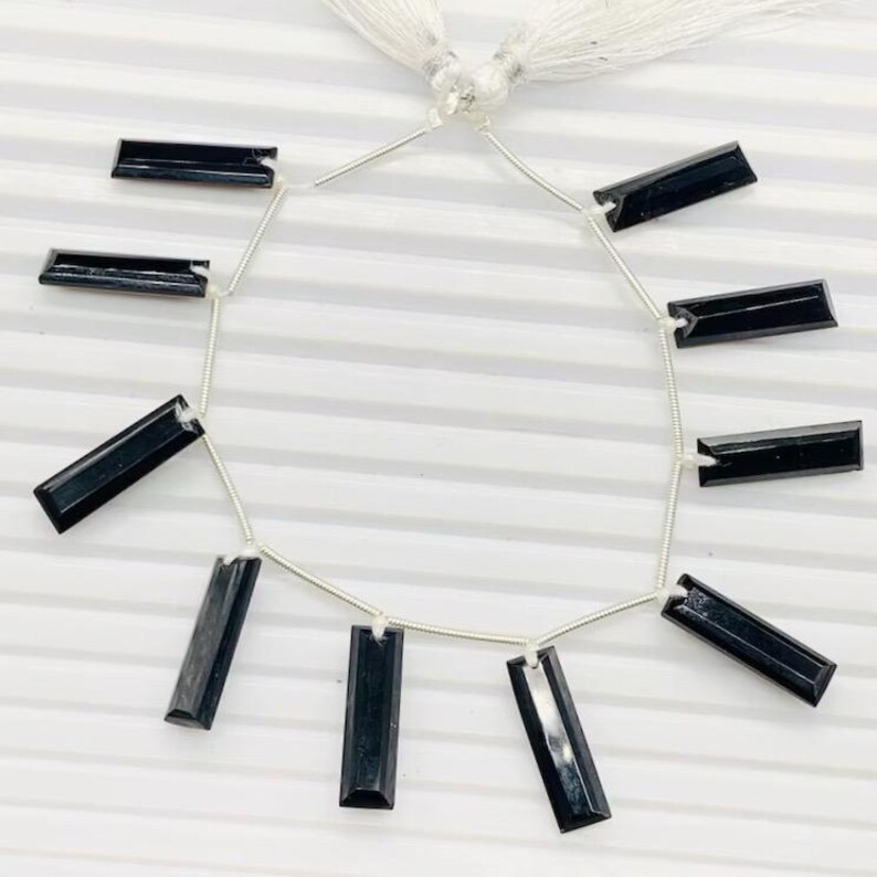 Pu&ograve; includere: Una collana di perle di pietre preziose nere, ogni perla &egrave; un prisma rettangolare con una finitura sfaccettata. Le perle sono infilate su un filo d'argento con un fiocco all'estremit&agrave;.