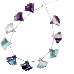 Op de afbeelding: Een streng met paarse, groene en blauwe fluorite edelsteen kralen in een waaiervorm. De kralen zijn geregen op een zilveren draad.
