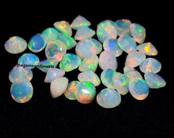 Pode incluir: Uma coleção de opalas facetadas com jogo de cores, incluindo azuis, verdes e laranjas. As pedras preciosas estão espalhadas sobre um fundo preto, mostrando suas qualidades iridescentes. A imagem inclui o texto "thegemsandjewels".