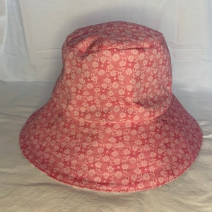 May include: A pink bucket hat with a white floral pattern.
