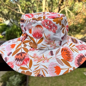 May include: A white bucket hat with a floral print featuring pink, orange, and brown flowers. The hat has a wide brim and a flat crown.