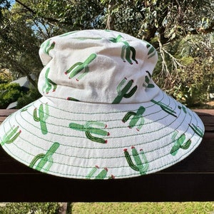 May include: A white bucket hat with a green cactus print. The hat has a wide brim and a flat crown.