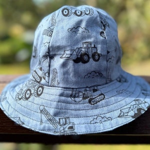 May include: A blue bucket hat with a black and white construction vehicle print. The hat has a wide brim and a flat crown.