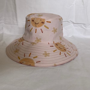 May include: A pink sun hat with a wide brim and a pattern of smiling suns and flowers.
